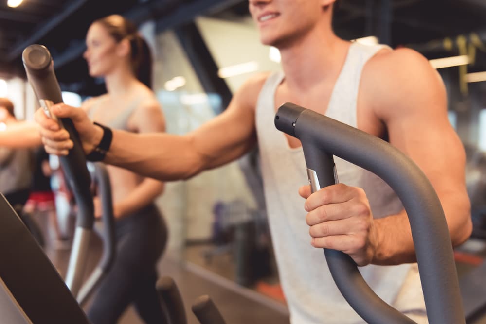 A muscular man working out on an elliptical trainer