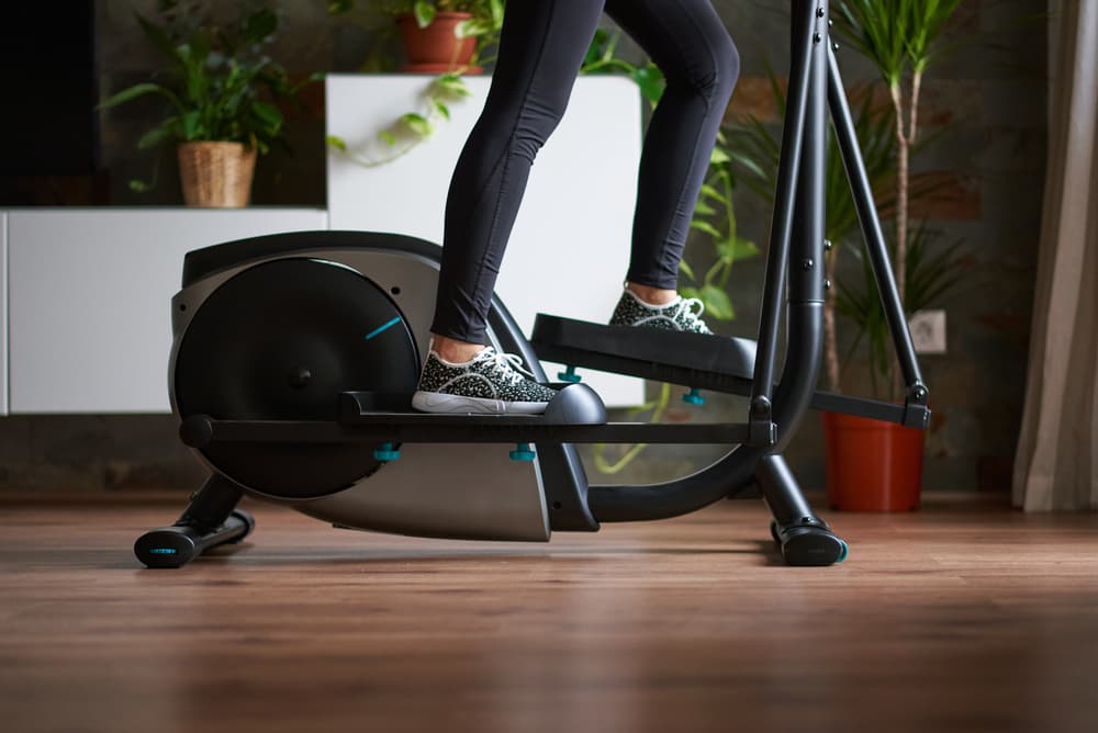 A pair of legs pedalling a rear drive elliptical cross trainer