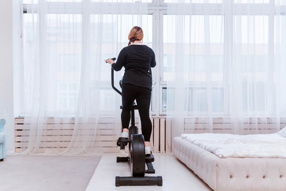 Back of a girl training on her elliptical machine in her bedtroom