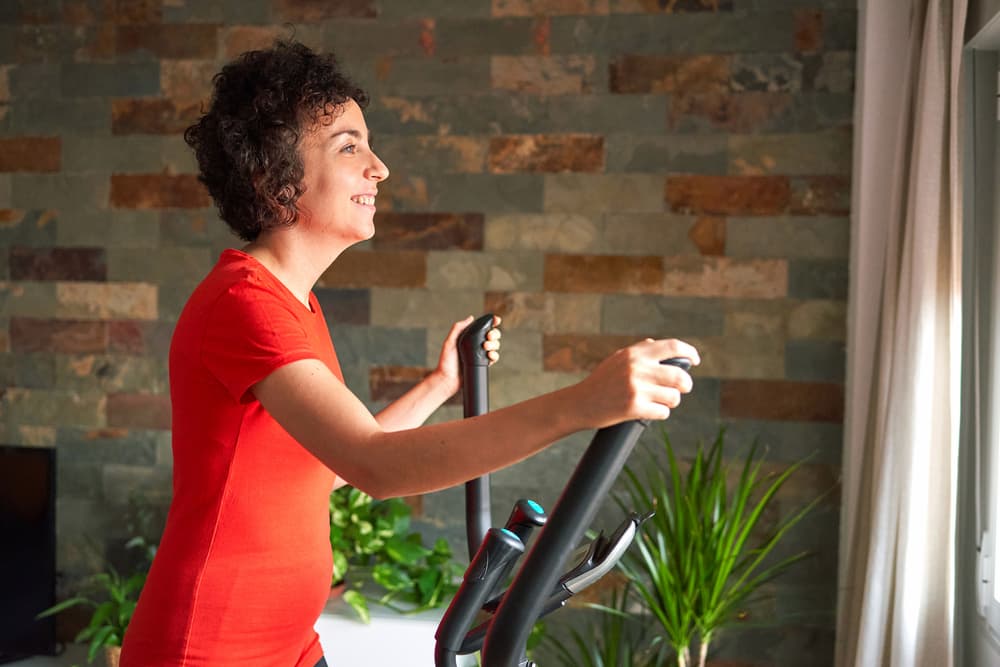 Side angle of the friendly woman training with her elliptical trainer